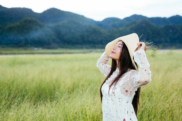 A woman who is holding a grass in her hands on a beautiful grass field with a mountain .