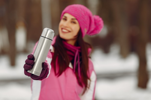 Free Photo woman in a winter park. lady in pink sportsuit. girl with a thermos.