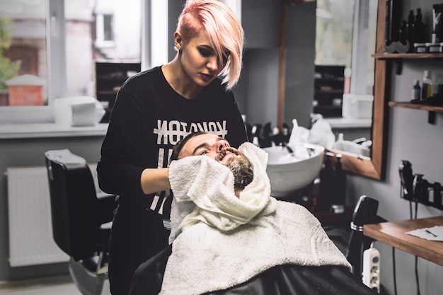 Woman wiping face of client in barbershop