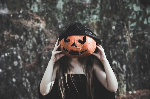 Free Photo woman in witch costume closing face by pumpkin