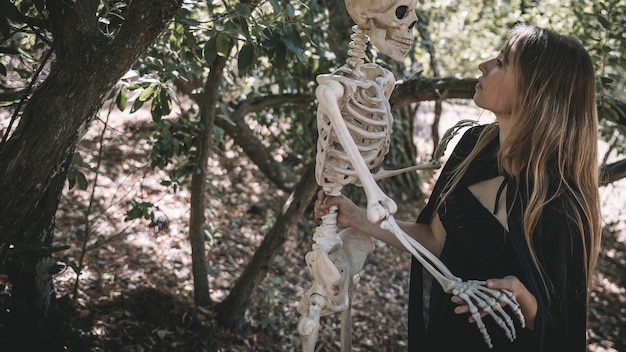 Free Photo woman in witch costume holding above head skeleton