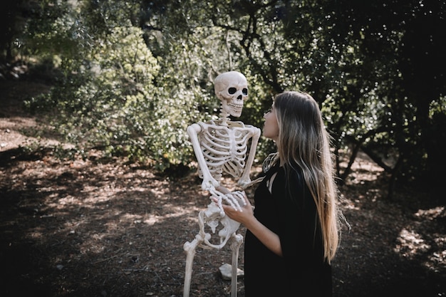 Free photo woman in witch suit holding and looking attentive at skeleton