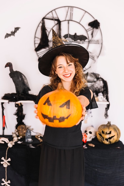 Free Photo woman in witch suit and pointy hat holding pumpkin and smiling