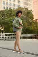 Free photo woman with afro hair dressed in hoodie leggings and sneakers has regular fitness training pses in urban setting exercises outdoors for keeping fit