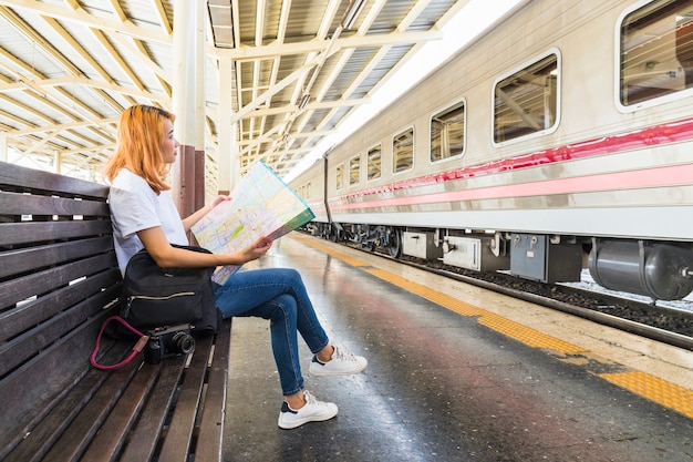 Free photo woman with backpack and map on bench on platform