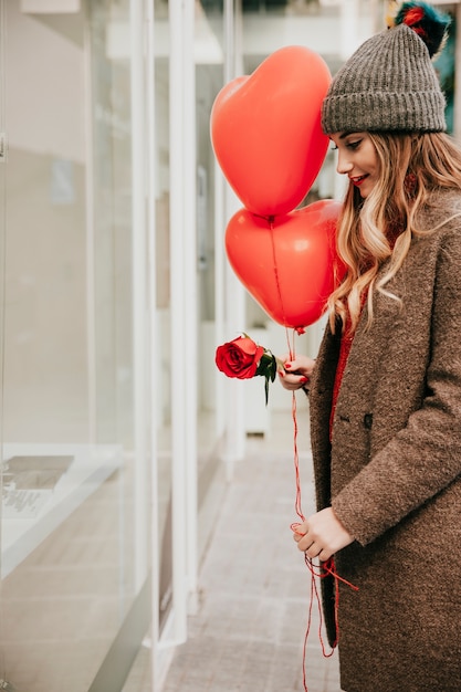 Free photo woman with balloons and rose near shop-window