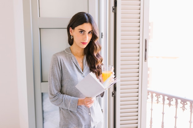 Free photo woman with book and juice near window