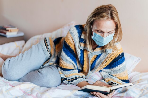 Woman with book and medical mask in quarantine at home