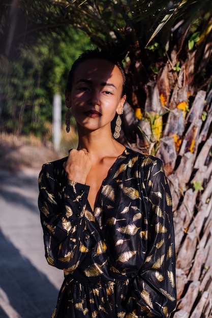 Free photo woman with bronze make up in black golden dress near a palm tree