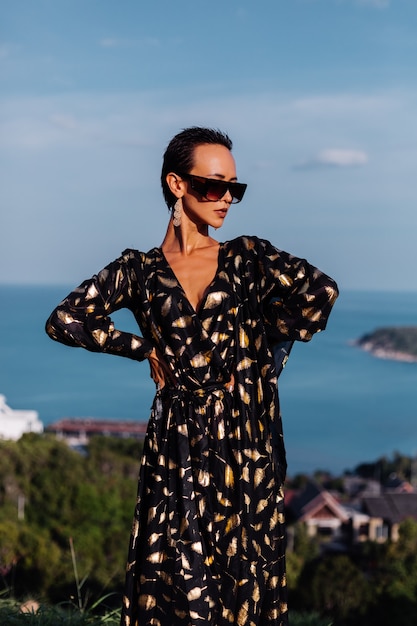 Free photo woman with bronze make up in black golden dress posing in seascape