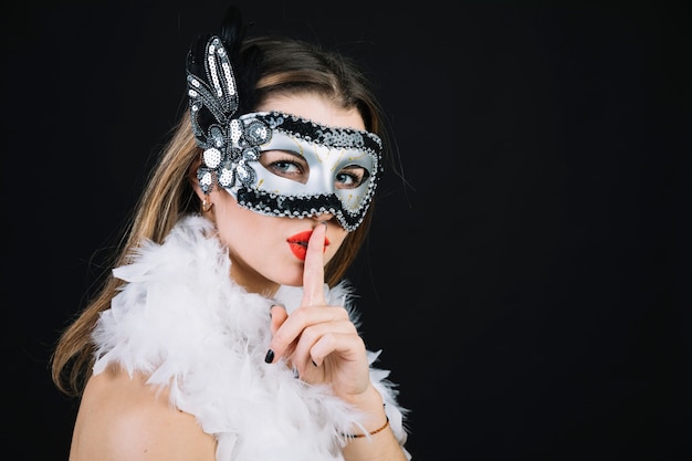 Free Photo woman with a carnival mask making silence gesture on black background