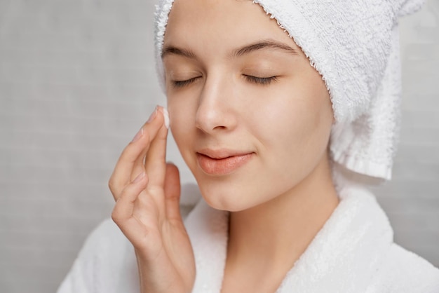 Free photo woman with closed eyes applying moisturizer on face