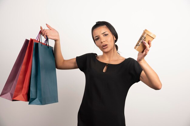 Woman with coffee and shopping bags feeling lost on white wall.