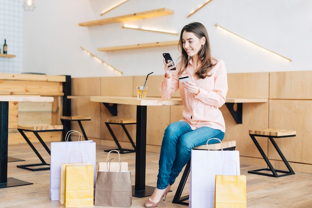 Woman with credit card using smartphone in cafe