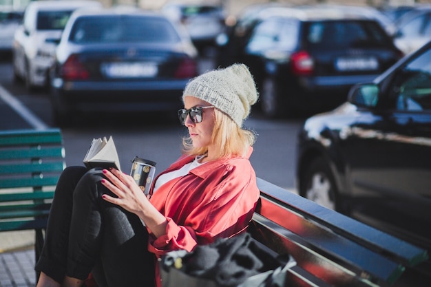 Free Photo woman with cup reading book on bench