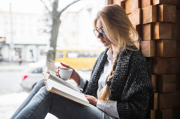 Free photo woman with cup reading near window