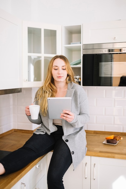 Free photo woman with cup using tablet in kitchen