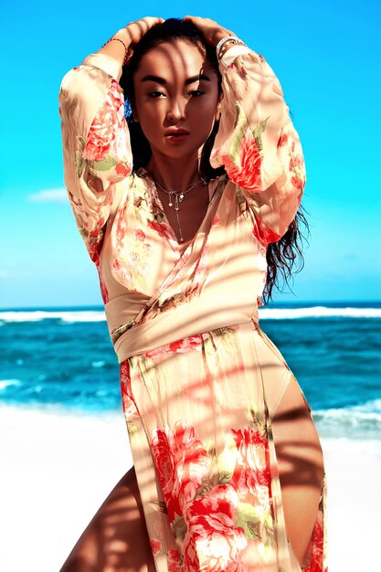 Woman with dark long hair in beige dress posing on summer beach