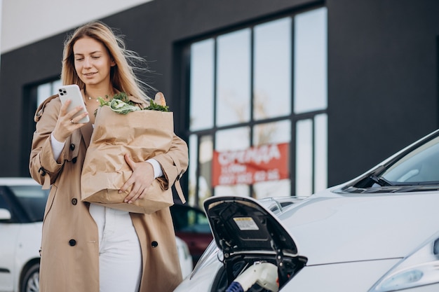 Free photo woman with food shopping bags charging electric car