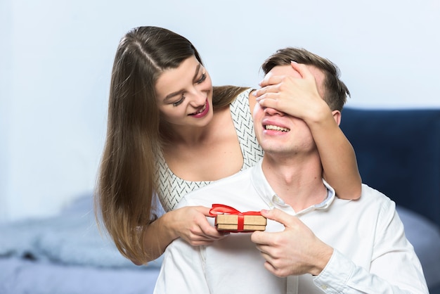 Woman with gift covering man eyes 