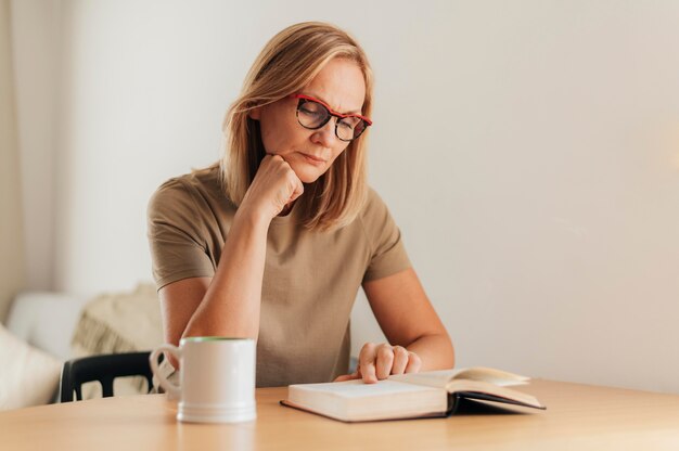 Woman with glasses at home reading book during quarantine