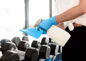 Free photo woman with gloves and cleaning solution disinfecting gym equipment