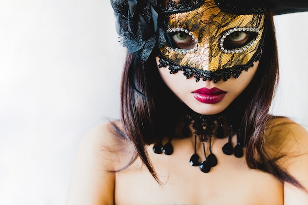 Woman with a golden venetian mask and a black hat on a white background