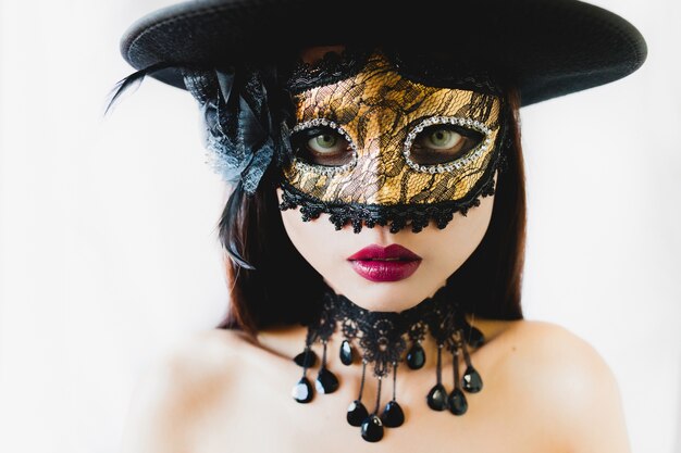 Woman with a golden venetian mask and a black hat on a white background