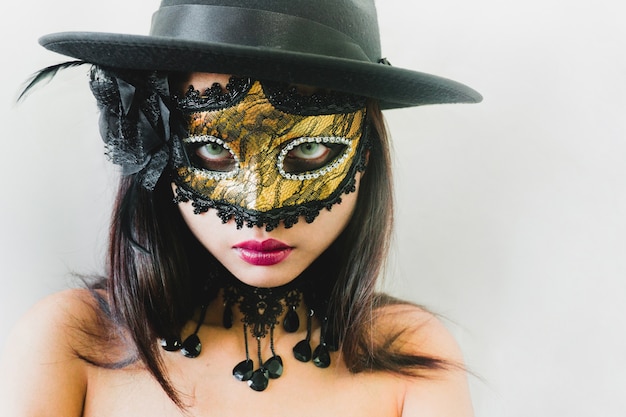 Woman with a golden venetian mask and a black hat on a white background