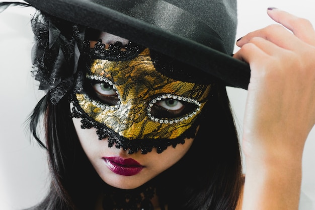 Woman with a golden venetian mask and a black hat on a white background