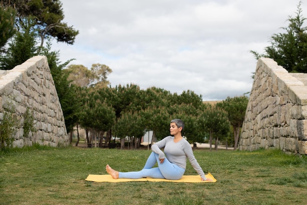 Free Photo woman with grey hair doing yoga in park. female model in sportive clothes exercising on mat on cloudy day. sport, hobby, health concept