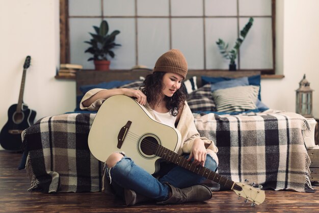 Woman with guitar in front of bed