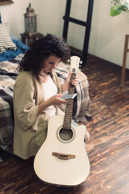 Woman with guitar and smartphone in bedroom