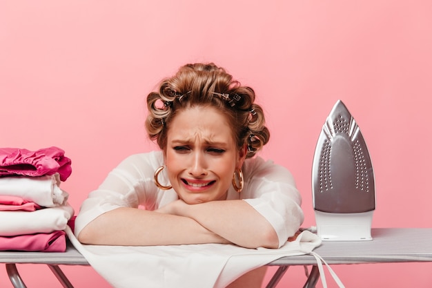 Free photo woman with hair curlers leans on ironing board and cries