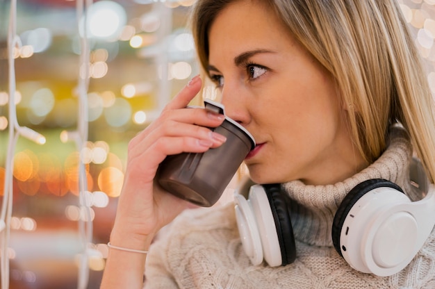 Free photo woman with headphones around the neck drinking out of cup