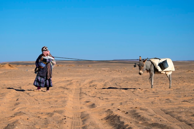 Free photo a woman with her child and donkey in the merzouga desert morocco