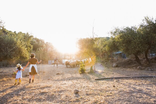 Woman with her daughter walking in the field with animals