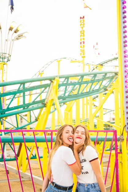 Woman with her friend sticking out tongue in front of roller coaster ride