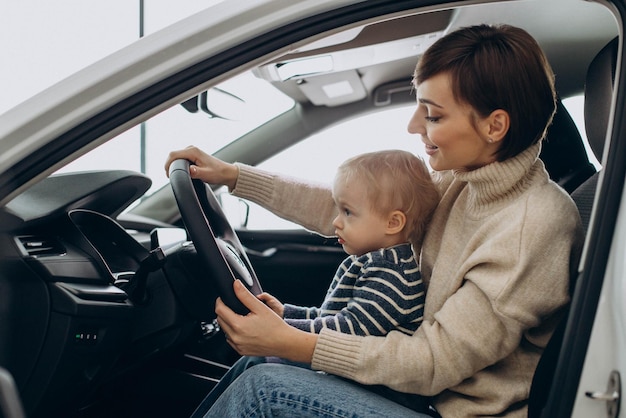 Woman with her little son holding steering wheel in a car in a car showroom