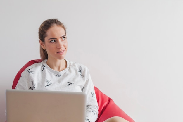 Woman with laptop on armchair looking to the side