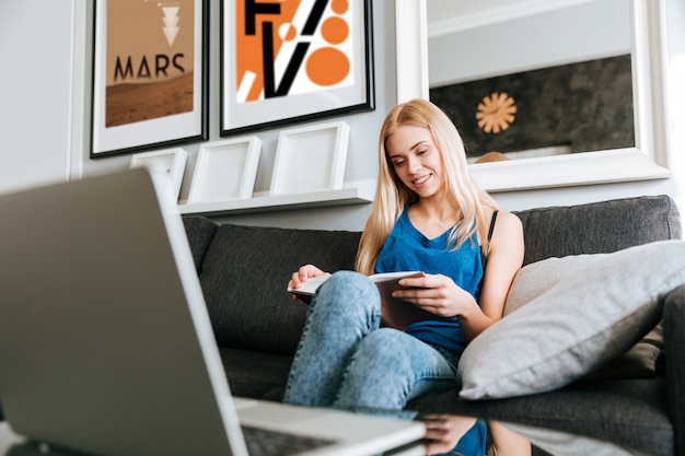 Woman with laptop on her table reading book at home