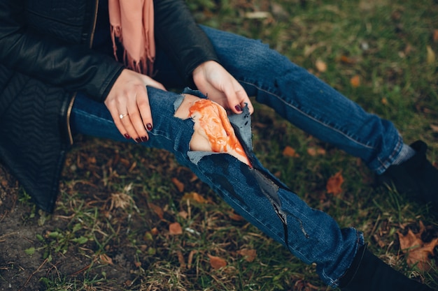 Free Photo woman with a leg injury. the wounded girl sitting by the tree. the wound is bleeding.