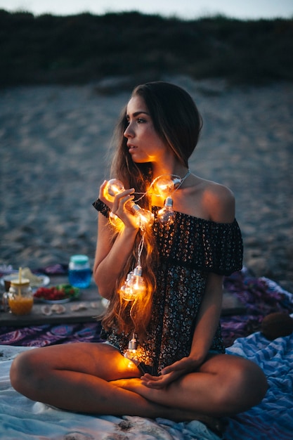 Free Photo woman with light bulb chain sitting at the beach