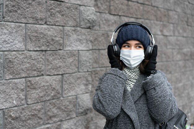 Woman with medical mask in the city listening to music on headphones