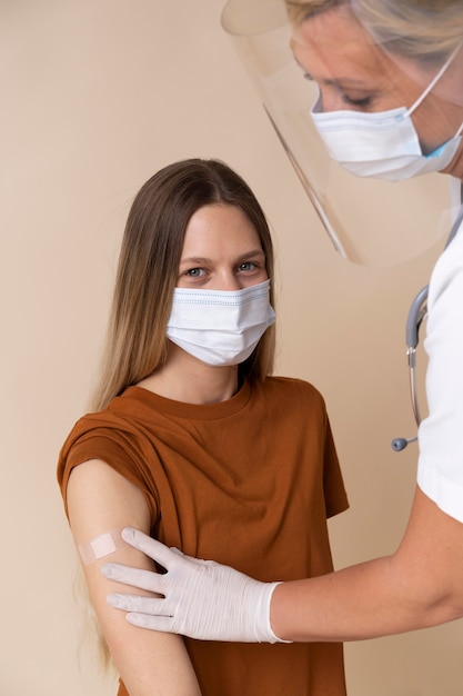 Free photo woman with medical mask getting sticker on arm after getting a vaccine