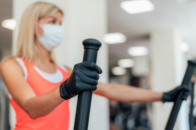 Woman with medical mask and gloves working out at the gym