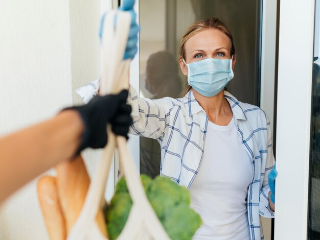 Woman with medical mask at home picking up her groceries in self-isolation