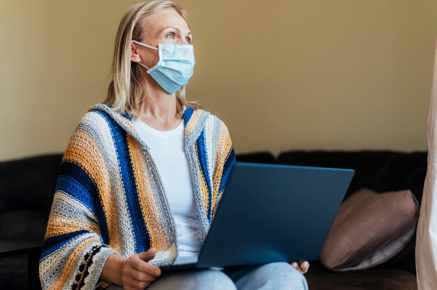 Woman with medical mask and laptop in quarantine at home