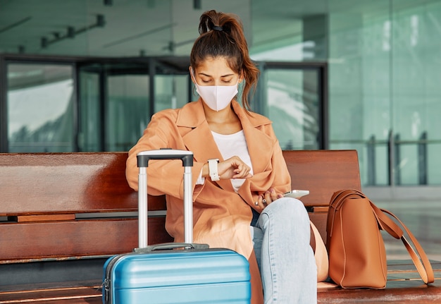 Free photo woman with medical mask looking at her watch at the airport during pandemic