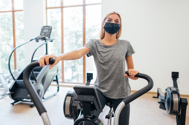 Woman with medical mask during pandemic exercising at the gym